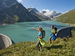 Kaprun Alpine Reservoirs - Couple with backpacks hiking at Mooserboden reservoir