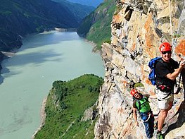 Kaprun High Mountain Reservoirs - men with climbing equipment at the via ferrata arena Hoehenburg with view of reservoir lake