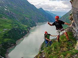 Kaprun Alpine Reservoirs - men with climbing equipment at the via ferrata arena Hoehenburg with view of reservoir lake